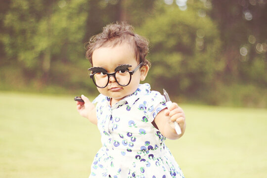 Portrait of a young girl with a moustache drawn on her face wearing novelty glasses with bushy eyebrows in a garden