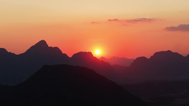 Stunning orange sky at sunset above limestone peaks of Laos from tripod aerial perspective. Paramotors outline in golden glow, savoring picturesque view