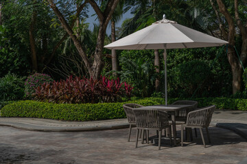 Obraz premium Summer Outdoor Garden Furniture with Sun Umbrella, Table and Wicker Chairs in Tropical Landscape Park, Luxury Relaxation and Vacation Concept