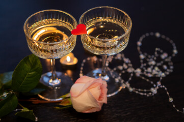 Romantic Valentine's Day still life with champagne glasses, pink rose, candles and red heart on dark background