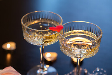 Romantic Valentine's Day still life with champagne glasses, pink rose, candles and red heart on dark background
