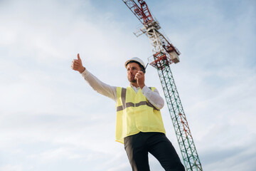 Obraz premium Controlling the process, with walkie talkie. Construction site worker is against building crane and sky background