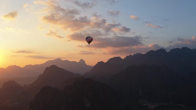 Hot air balloons flying over Vang Vieng town in Laos with karst mountains background during scenic golden hour sunset