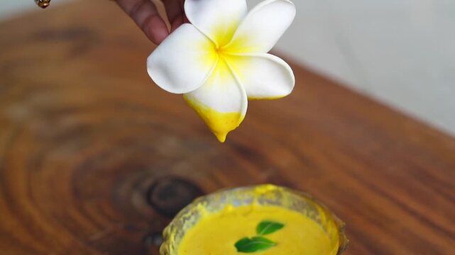 Organic ubtan facial in bowl close up on a wooden background. Champa flower petals and natural face mask cosmetic concept. Homemade natural skincare product for beauty treatment. Ayurvedic paste