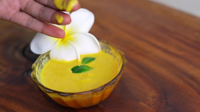 Organic ubtan facial in bowl close up on a wooden background. Champa flower petals and natural face mask cosmetic concept. Homemade natural skincare product for beauty treatment. Ayurvedic paste
