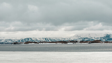 Fototapeta premium partially frozen lake next to mountains and hills covered with snow in iceland