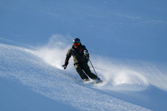 Skier carving a turn on a snowy mountain slope, mastering off-piste freeride technique
