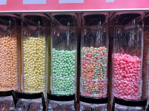 Close-up of colorful candies in clear plastic dispensers at a candy shop, bulk confectionery display background