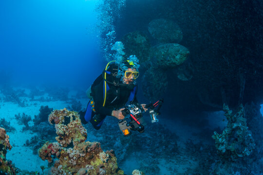 Scuba diver with underwater camera explores the interior of the sunken ferry Salem Express in the Red Sea. Historic shipwreck covered with coral and marine growth, Egypt.