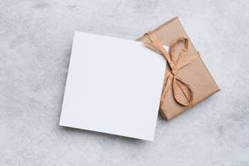 Blank greeting card mockup with craft paper gift box over grey background, copy space for any occasion congratulations text