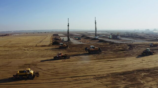 Construction work is underway on a new site with heavy machinery operating in an open area during the day