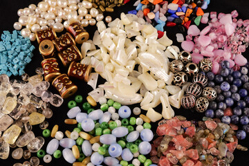 A variety of beads made of natural stone, glass, mother-of-pearl, ceramics and metal on a black background	