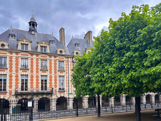 Beautiful Place des Vosges with trees and old historical buildings in background. Paris, France.