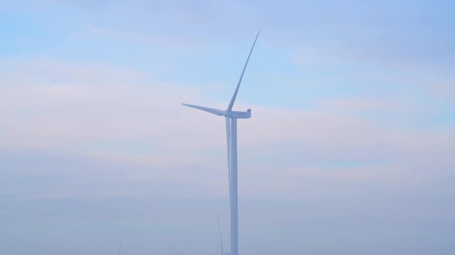 Wind turbines on open farmland under a soft overcast sky, surrounded by misty air and flat terrain, highlighting clean energy development in a peaceful rural setting