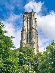 View of a tower Tour Saint-Jacques through the branches of flowering trees against a cloudy sky in Paris, France.