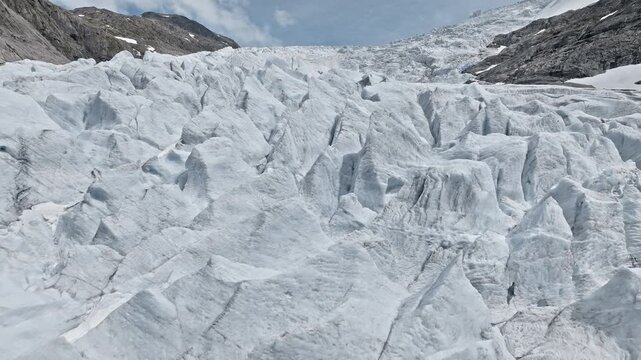 Wide close-up of Briksdalsbreen glacier ice field in Norway. Drone captures jagged frozen formations and textured ice under clear summer skies.