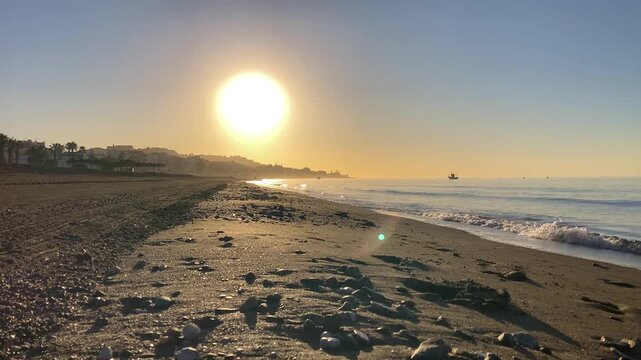 Stunning sunset illuminates the beach and rocky coastline near the &ldquo;El Cantal&rdquo; tunnels in Rincon de la Victoria, Spain, painting the sky in warm golden hues.