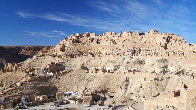 Panorama: Chenini ksar at golden hour in southern Tunisia, ancient Berber village with white mosque and stone houses on desert hill, dramatic light, heritage, travel destination