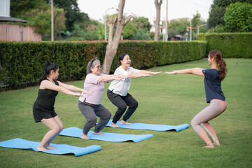 Group of older Asian women doing yoga squat exercise on mats in green park with young female instructor. Healthy lifestyle, senior fitness and outdoor wellness activity.