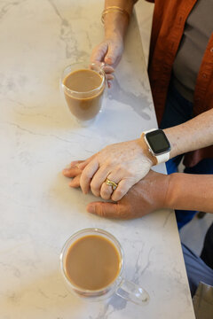 Hands clasping on marble counter while hand reaching for two mugs, gold ring and square watch