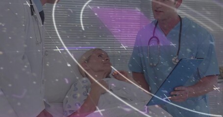 Lying patient wearing patterned gown getting care from staff in hospital room blue scrubs clipboard