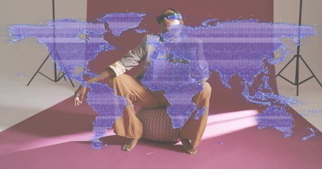 Sitting Indian model wearing shades, posing on pouf in studio with purple world map overlay casting © vectorfusionart