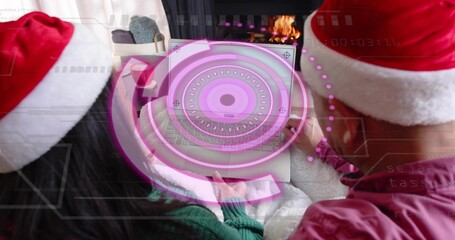 Naklejka premium Holding couple wearing Santa hats sharing laptop on couch, displaying magenta holo UI and fireplace