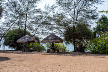Seating under a wooden hut shelter, located by the sea.