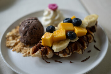 Waffle with chocolate ice cream served with sliced banana and mango, whipped cream and sauce.