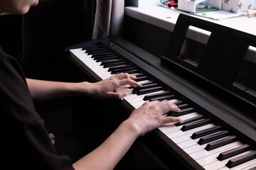 Fototapeta premium A pair of hands plays a sleek black piano keyboard. Soft lighting highlights the fingers pressing the white and black keys, creating a moody, artistic atmosphere. Close-up shot, dark background.