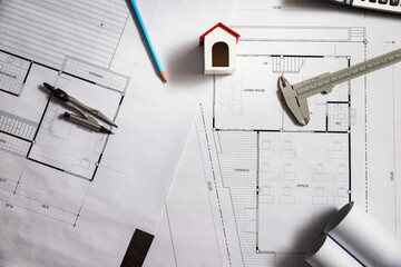 Top view of architectural construction plan with house model and engineering tools. Workplace concept with blueprint, vernier caliper, and pencil on desk.