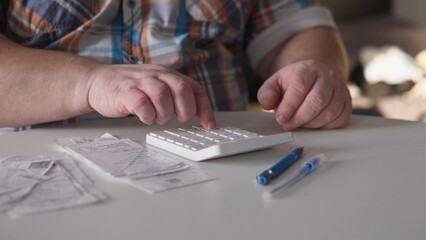 Fototapeta premium A person is pressing buttons on a calculator at a table. Receipts are scattered on the table along with two pens. The setting has soft lighting and a relaxed atmosphere.