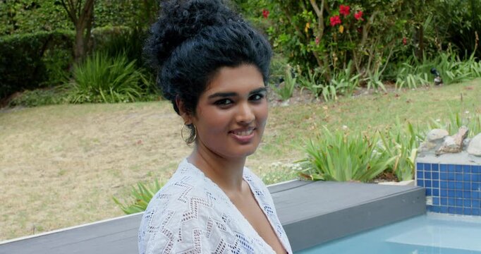 Adult female sitting poolside in white crochet cover-up, blue swimsuit, on cue turning and smiling