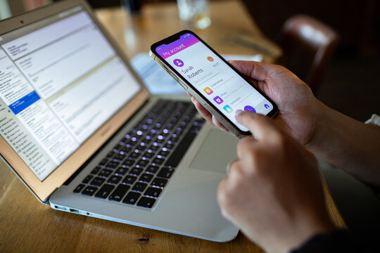 Person using account app on smartphone beside laptop at home