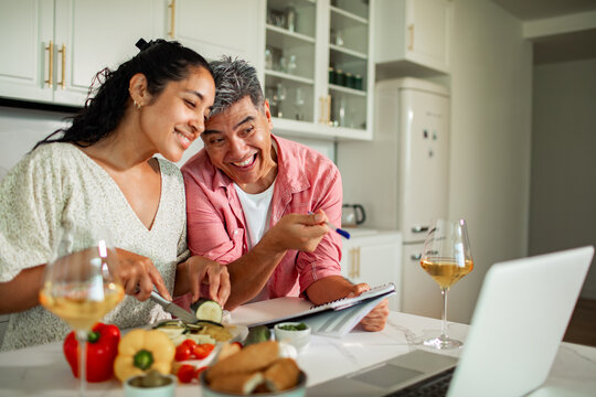 Smiling couple cooking together in home kitchen while following online recipe
