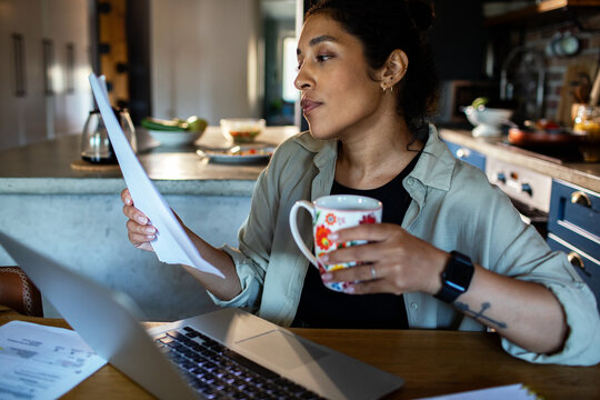 Woman reviewing bills with coffee at home kitchen table