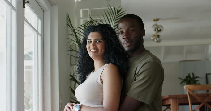 Couple African American man moving behind and embracing Indian woman at window, smiling, smartwatch