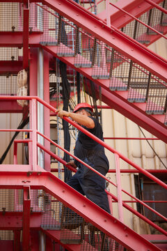 Worker in safety helmet on red industrial stairs. Ideal for: workplace safety brochures, energy plant maintenance reports, and industrial labor articles.