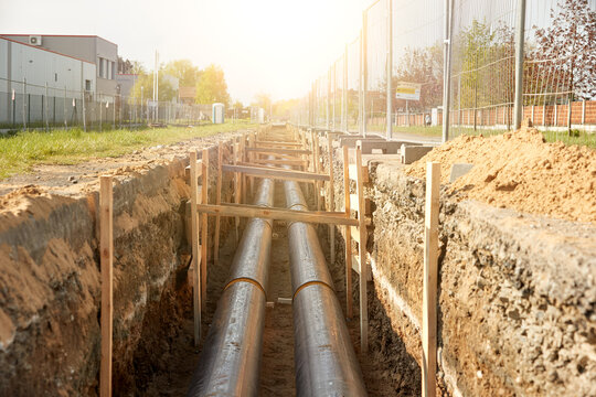 Industrial site showcasing the installation of pre-insulated steel pipelines in a trench. Ideal for: district heating project reports, energy efficiency articles, and utility maintenance news.