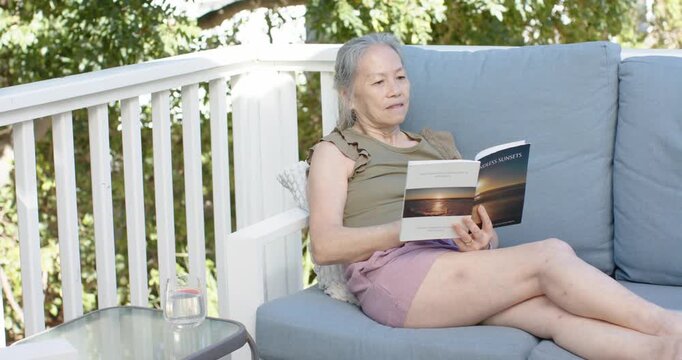 Sunlight is nudging senior woman into reclining reading book and turning pages on balcony to relax