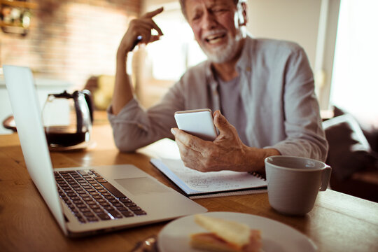 Senior man struggling with smartphone at home office