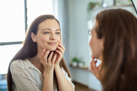 Young woman checking skin in bathroom mirror
