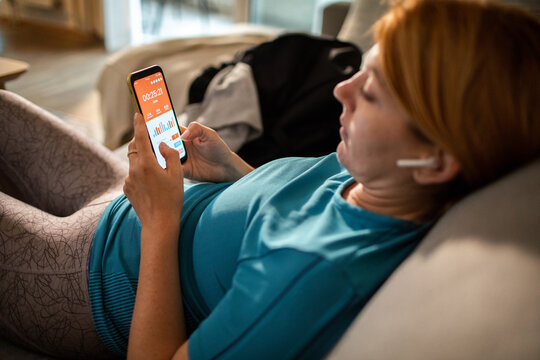 Woman checking fitness app on smartphone while resting on sofa at home