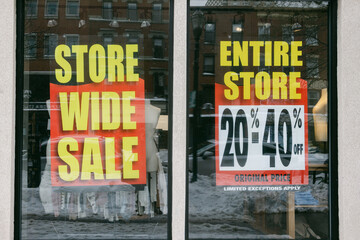 Store wide sale takes place in downtown area during winter season with discounts displayed on storefront windows