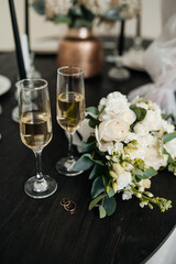 A bridal bouquet of white roses next to two glasses of champagne