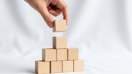 A hand building a pyramid with wooden blocks on a white surface