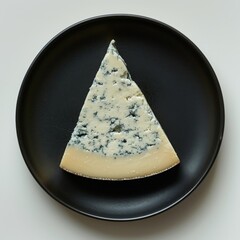 top down view of a black dinner plate with a slice of gorgonzola cheese