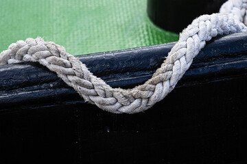 Fototapeta premium Close up of a braided rope handle attached hanging on a black boat side with a green textured floor 