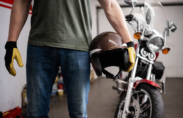 Fototapeta premium Man Holds A Protective Moto Helmet Against A Classic Motorcycle In A Garage