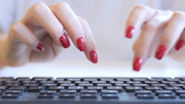 Woman is typing on a keyboard with her fingernails painted red. She is using the number pad and the shift key